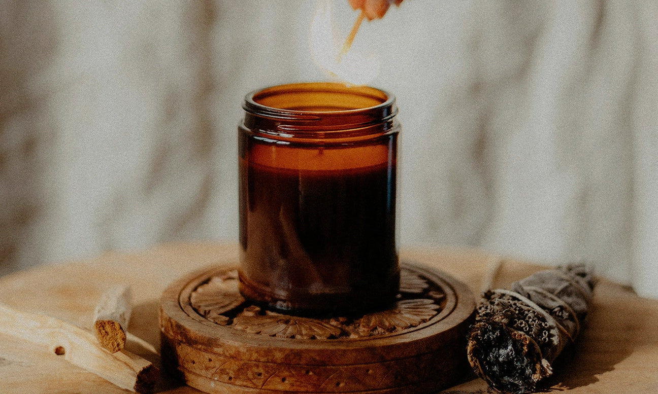 Hand lighting a candle ritual for manifestation, love and healing. Palo santo and energy cleansing bundle nearby