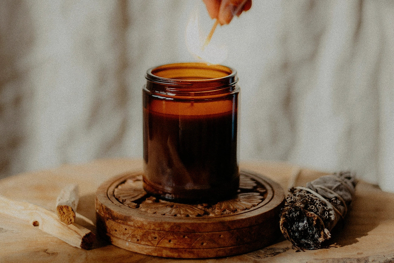 Hand lighting a candle ritual for manifestation, love and healing. Palo santo and energy cleansing bundle nearby